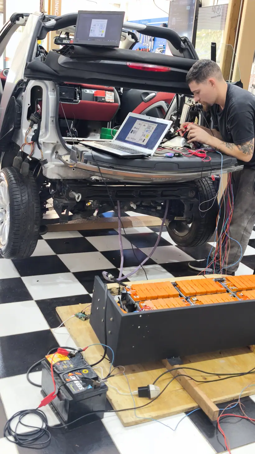 El pack apoyado en el piso conectado al auto abierto, con notebook y batería auxiliar de 12 V