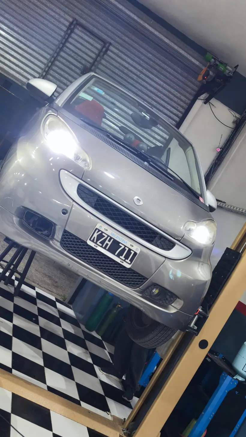 El Smart de frente con las luces prendidas en el taller